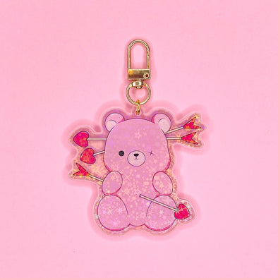 Acrylic keychain with star holographic finish and gold key ring. Artwork shows a super cute pink teddy bear missing an eye button with heart arrows through it.
