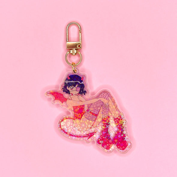Acrylic keychain with star holographic finish and gold key ring. Artwork shows a super cute devil girl with red horns, wings, and tail, and a matching red bodysuit and boots.