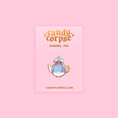 Enamel pin of a ghost in a teapot. Sitting on a pink backing card with gold foil Candy Corpse logo.